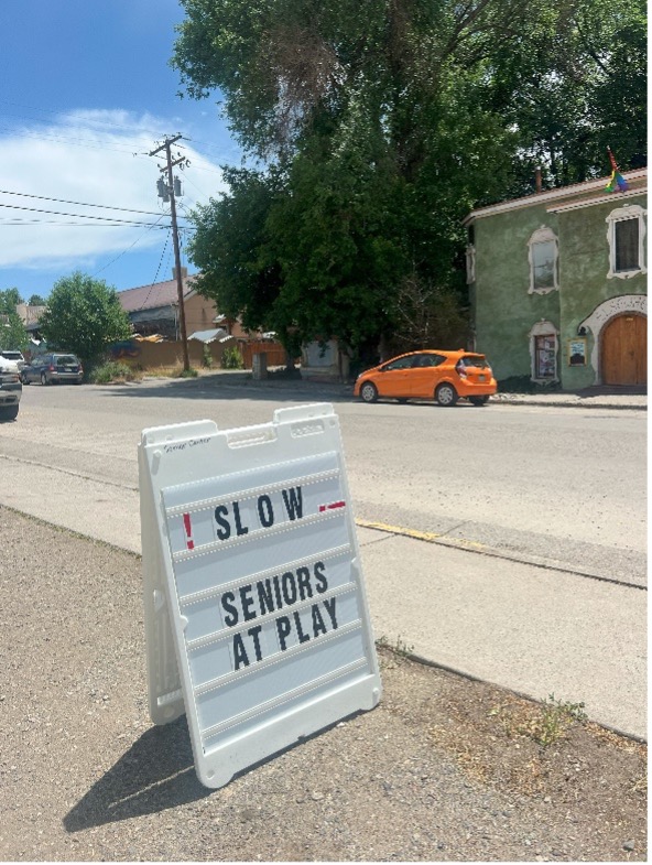 A frame sign stating "Slow Senior at Play" in black font on a street