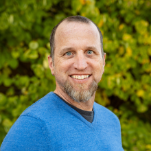 Man in blue shirt in from of a tree smiling